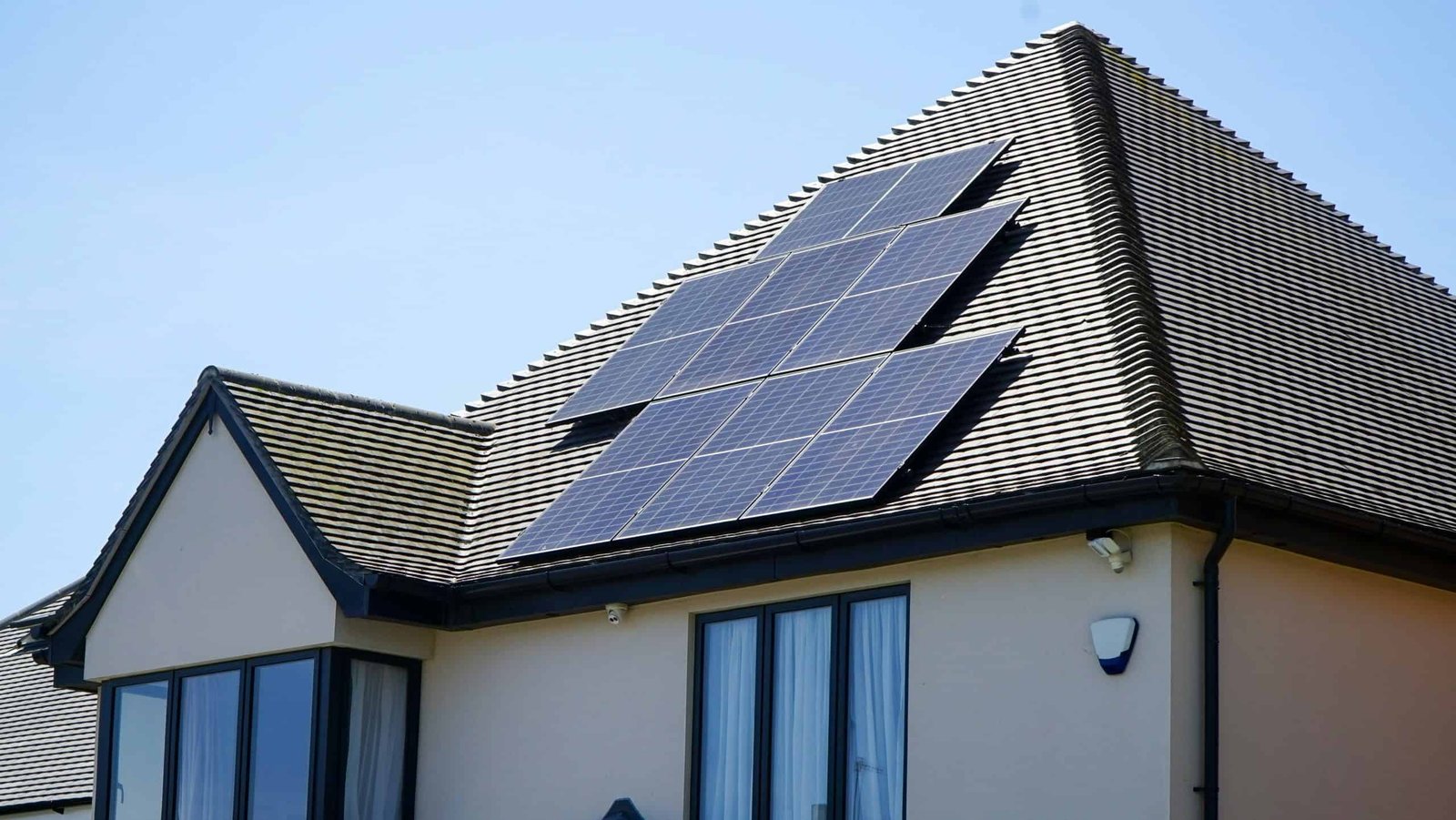 Vue extérieure du toit d'une maison moderne équipé de plusieurs panneaux solaires photovoltaïques sous un ciel bleu dégagé.